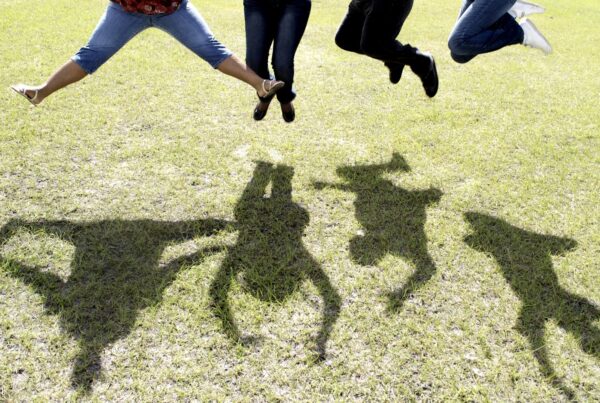 A photo of the feet of people jumping -- their shadows are shown in full on a green lawn.