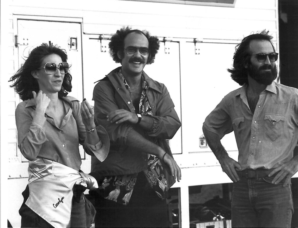 A black and white photo of three people standing in the wind.