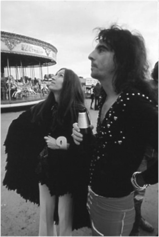 A black and white photo of two people with a ferris wheel in the background.