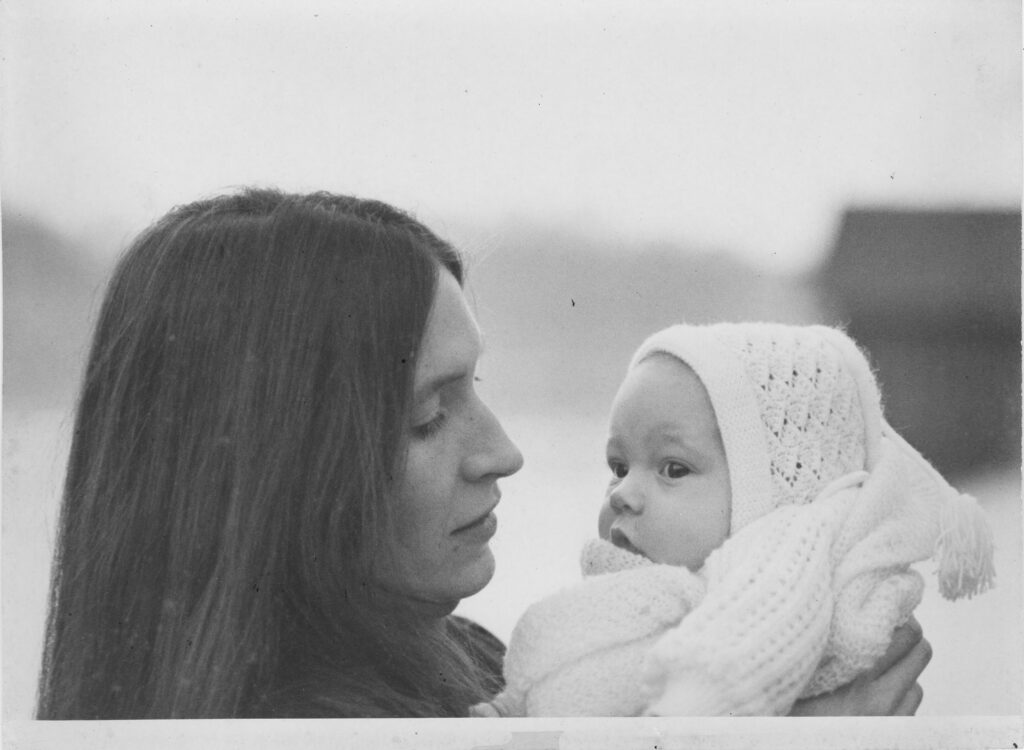 A black and white photo of a woman holding an infant dressed in knitted clothes.