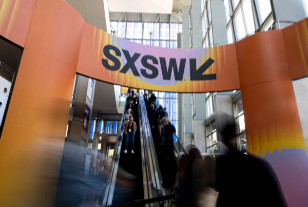 A large orange, purple and yellow sign stretching across two escalators that says "SXSW" in large black letters