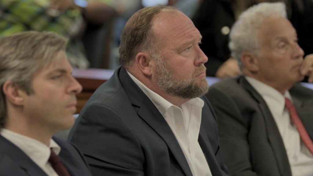 A photo of Alex Jones seated in between lawyers in a courtroom.