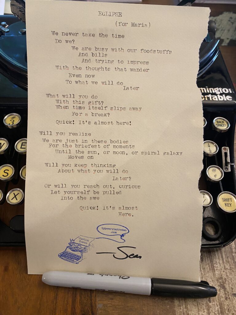 A photo of the typewritten poem on a torn half sheet of light yellow paper. The paper rests upright on the vintage, manual typewriter it was typed on. In front, is the marker the poet used to sign his name on it.