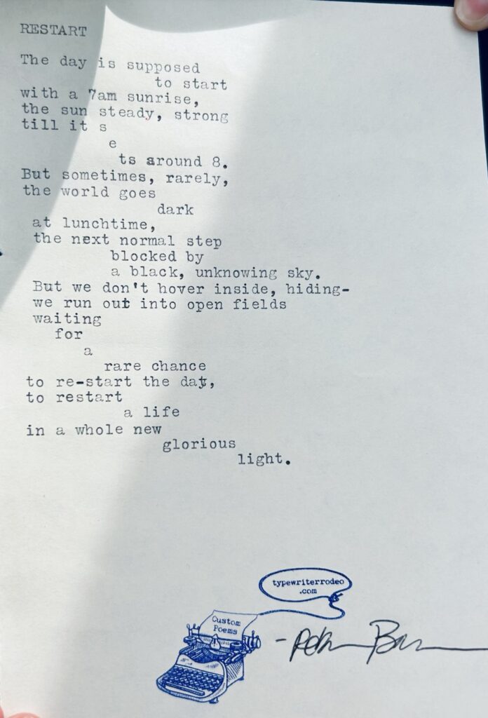 A photo of the typewritten poem on a half sheet of paper. The poem is held in the sunlight with shadows cast on it.