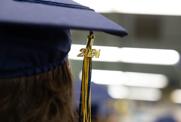 A close-up of a blue graduation cap with a blue-and-yellow tassel that has a "2024" charm on it
