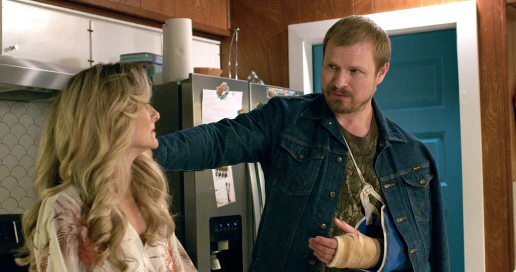 A still image from the film "Leads" shows two actors having a conversation in a kitchen. One has an arm in a sling.