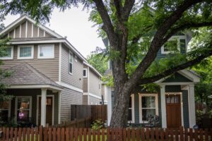 A two-story grey house next two a two-story blue house with a large tree in front of it.