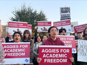 Students in a group at an outdoor rally hold maroon and white signs reading "Aggies for Academic Freedom."