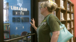 A photo of Baker looking through an internal window into an office. The word "librarian" is printed in white on the window.