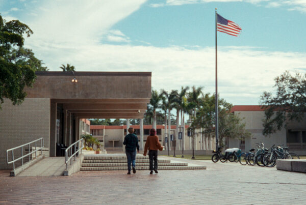 Two people walk on a college campus in a still image from the film "First They Came for My College: