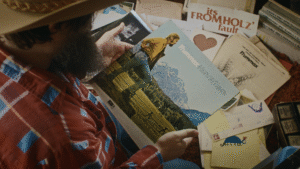 A still image from the film "The Man with the Big Hat" shows a person looking at the obscure debut album of Steven Fromholz.