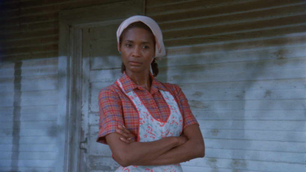 A Black woman stands with her arms crossed outside of a home.