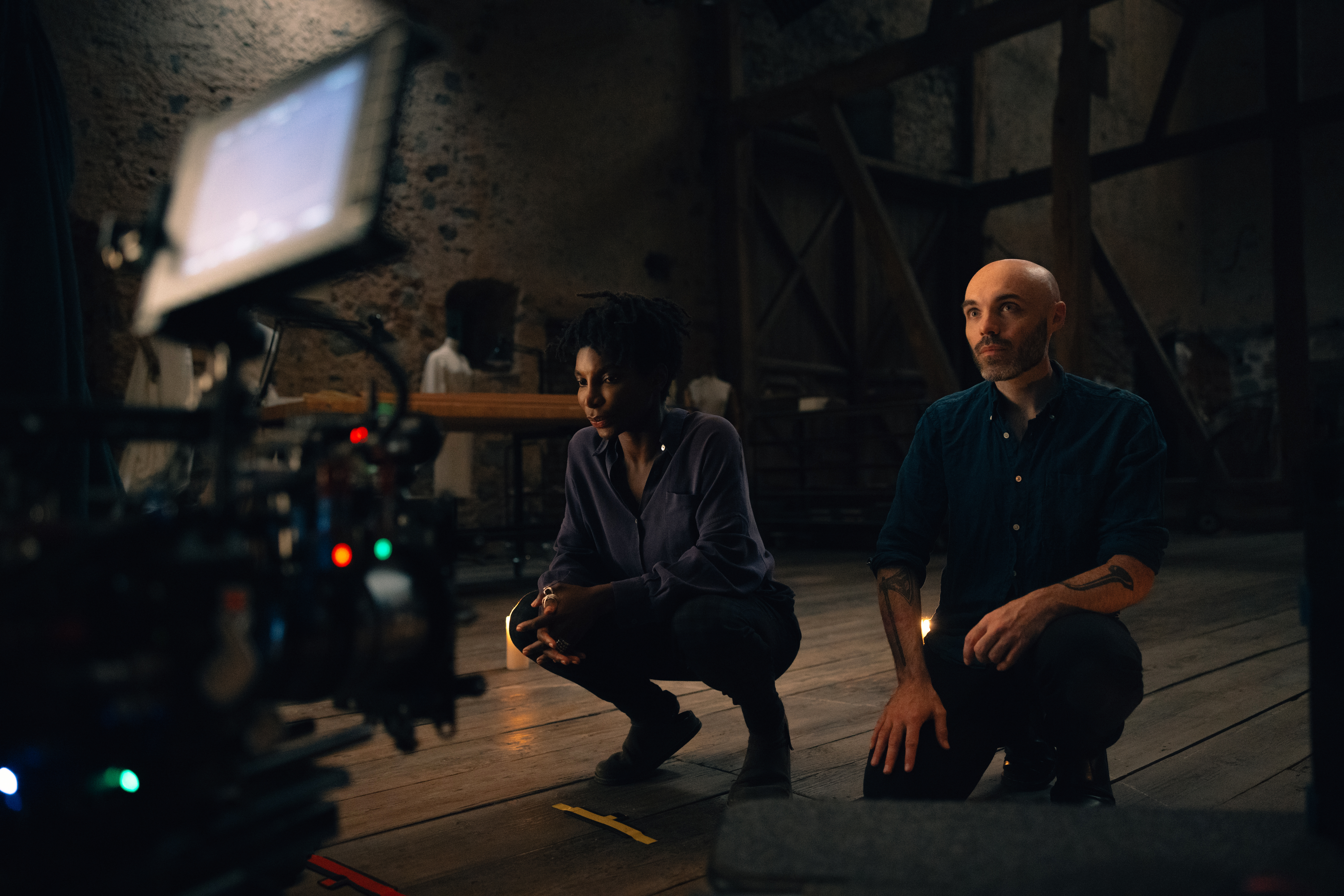 A behind-the-scenes photo shows actress Michaela Coel and director David Lowery squatting on a floor and looking at a monitor.