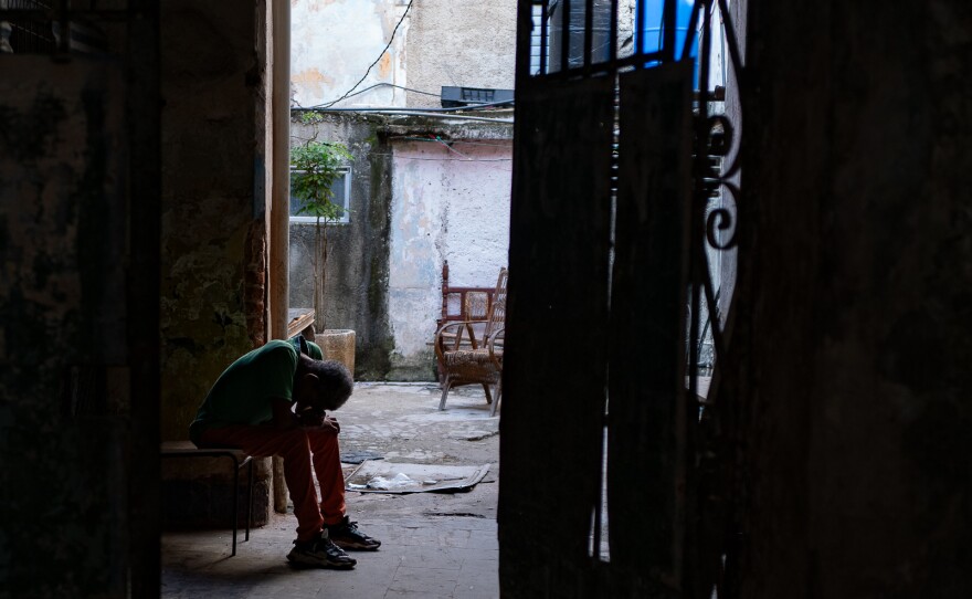 A person is in silhouette with their head on their knees in an alleyway in Havana.