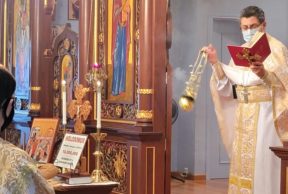 a priest wearing a white and gold robe reading from a red bible and waving an incense ball