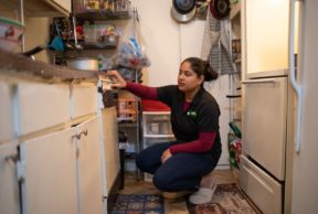A woman kneels down in her kitchen facing the dishwasher